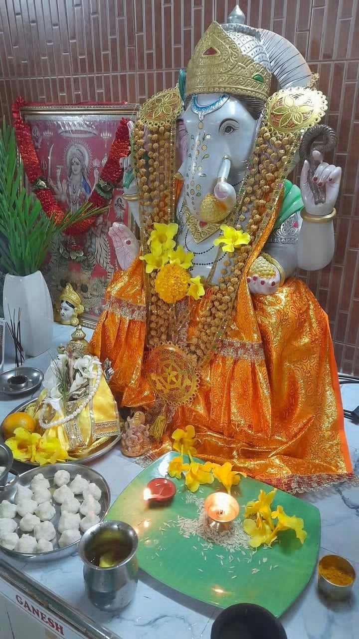 Statue de Ganesh habillée et fleurie, avec offrandes et diyas allumés